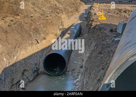 Verlegung von Engineering- und Heizungsanlagen; schwarze Kunststoffrohre befinden sich im Erdgraben. Stockfoto