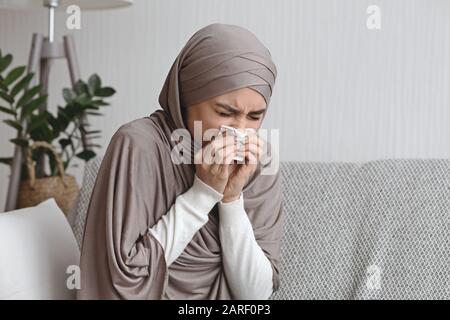 Kranke muslimische Frau bläst zu Hause die laufende Nase zur Serviette Stockfoto