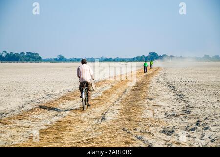 Radfahrer auf ihrem schwierigen Weg in die Dörfer auf der sandigen Insel Majuli, nachdem sie den Fluss Brahmputra mit lokalen Fährschiffen überquert haben Stockfoto