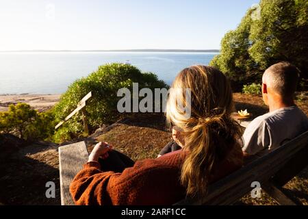 Reifes Paar, das vor dem eigenen Haus sitzt und einen schönen, hellen Blick auf den Strand und das Meer in Australien hat. Stockfoto