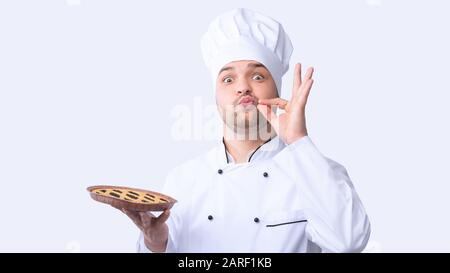 Chefkoch Guy Holding Pie Doing Zip Your Lip Gesture, Studio Stockfoto