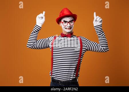 Fröhlicher MIME in rotem Hut und Weste mit Daumen oben auf leerem orangefarbenem Hintergrund Stockfoto