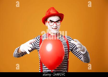 Clown MIME mit rotem Ball auf leerem orangefarbenem Hintergrund Stockfoto