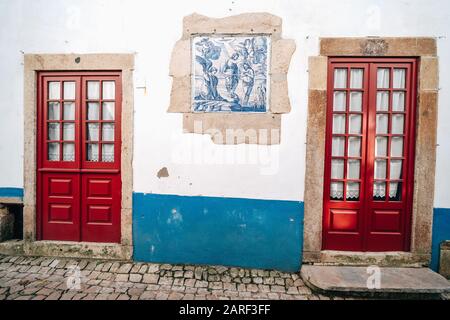 Traditionelle rote Türen mit weißen Wänden und blauen Akzenten in Obidos Portugal Stockfoto