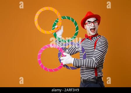 Fröhlicher MIME mit mehrfarbigen Ringen auf leerem orangefarbenem Hintergrund Stockfoto