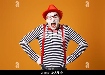 Junger MIME-Mann mit weißen Handschuhen und rotem Hut auf leerem orangefarbenem Hintergrund Stockfoto