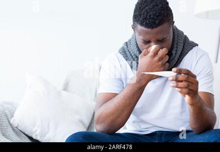 Kranker afroamerikanischer Kerl, der Thermometer hält und Fieber hat Stockfoto