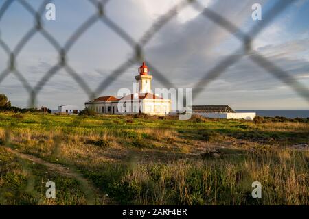 Leuchtturm von Alfanzina, in der Dämmerung durch einen Kettengliedzaun geschossen. Der Leuchtturm ist umgeben von Zäunen, in der Nähe der Stadt Carvoeiro Stockfoto