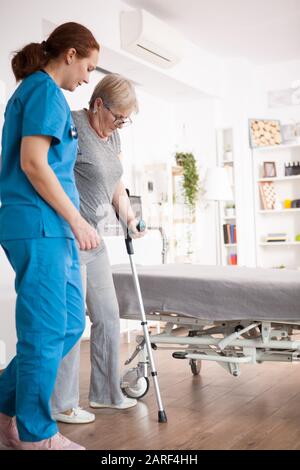 Krankenschwester hilft alten Frauen bei Gehproblemen im Pflegeheim mit Krücken. Stockfoto