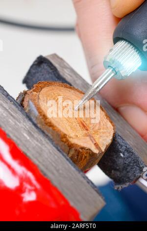 Frau, die ein schnelles Drehwerkzeug verwendet, um Schmuck auf einer Holzscheibe zu gravieren. Das Werkzeug kann als Mahlwerk verwendet werden Stockfoto