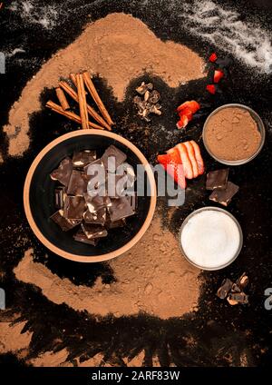 Schüssel mit Schokoladenstücken Schüssel mit Zucker und Kakao mit Erdbeeren und Zimt, auf schwarzem Grund Stockfoto