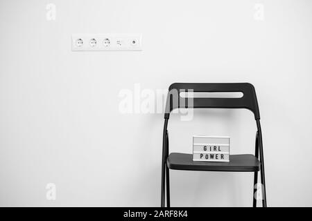 Mädchen Power Text auf dem Leuchtkasten. Weiße Wand und Steckdosen. Blsck Stuhl Stockfoto