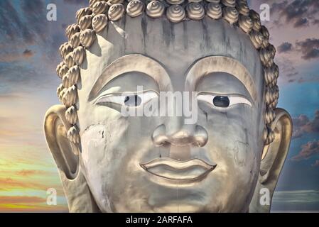 Dieses einzigartige Foto zeigt den goldenen Kopf einer großen Buddha-Statue und einen verträumten Sonnenuntergang mit roten Wolken am Himmel von Hua hin in Thailand. Stockfoto