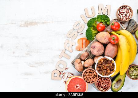 Lebensmittel, die natürliches Kalium enthalten. K: Kartoffeln, Pilze, Banane, Tomaten, Nüsse, Bohnen, Brokkoli, Avocados. Draufsicht. Auf weißem Holzhintergrund. Stockfoto