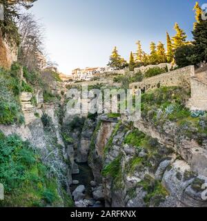 Ronda, Spanien: Landschaft der weißen Häuser am grünen Rand der steilen Klippen mit Bergen im Hintergrund. Stockfoto