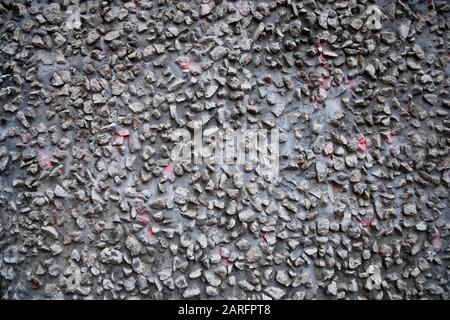 Graue, körnige Wandtextur mit darin integrierten Schottersteinen Stockfoto