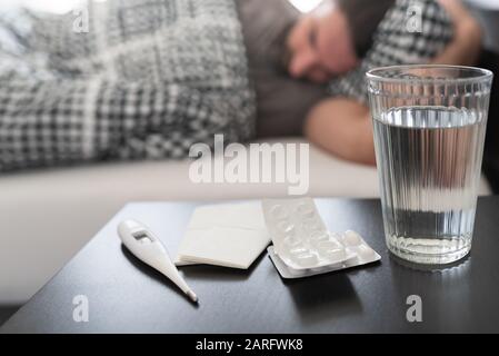 Med, medizinisches Thermometer und Glas Wasser auf Nachttisch gegen kranke Menschen, die an Grippe leiden oder im Bett schlafen Stockfoto