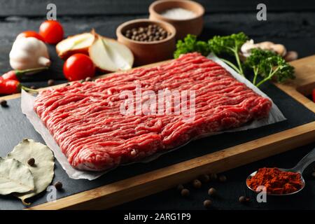 Gewürze und Schneidebrett mit Hackfleisch auf Holzgrund, Nahaufnahme Stockfoto