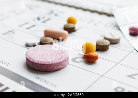 Pillen, Ergänzungen und Medikamente für die Krankheit. Ein Haufen verschiedener Pillen auf einem Kalenderhintergrund. Gesundheitswesen Stockfoto