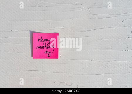 Handschriftertext auf Memo-Post-Erinnerung. Fröhlicher Muttertag auf Papier, an weißer und strukturierter Wand. Kopierbereich. Stockfoto