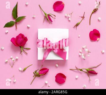 Weiße Geschenkbox und pinkfarbene Rosen auf hellrosa Hintergrund Draufsicht Stockfoto