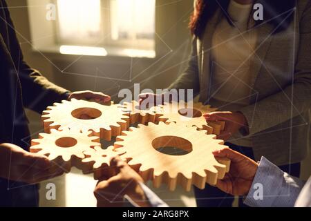 Eine Gruppe von Geschäftsleute hält Holzräder mit Zähnen in den Händen auf einem weißen Tisch im Büro. Stockfoto