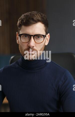 Junger Geschäftsmann im Amt. Business-Porträt eines hübschen bärtigen Mannes, der Brillen trägt, die am Arbeitsplatz sitzen. Selbstbewusster Geschäftsmann wurde Stockfoto