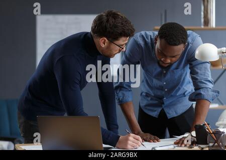 Multiracial Engineer Team arbeitet im Büro mit blauen Drucken und Architektengeräten, die Bauvorhaben skizzieren, diskutieren und planen. Partner Stockfoto