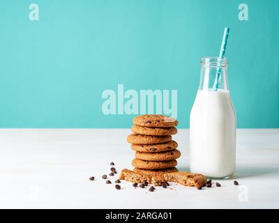 Haferflocken mit Schokoladentropfen und Milch in der Flasche, gesunder Snack. Heller Hintergrund, hellblaue Wand Stockfoto