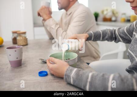 Mädchen gießt Milch in einen Teller mit Haferbrei. Stockfoto