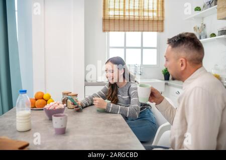 Vater und Tochter sitzen nach dem Frühstück am Tisch in der Küche. Stockfoto