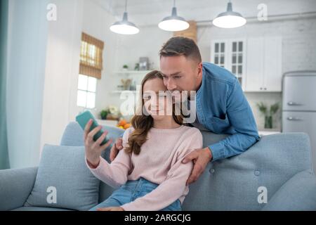 Papa mit Tochter sieht sich den Smartphone-Bildschirm zufrieden an. Stockfoto