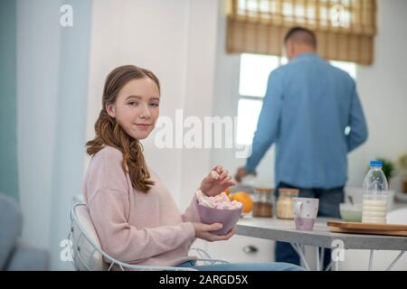 Glückliche Tochter sitzt mit Marshmallows in der Küche am Tisch. Stockfoto