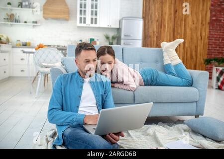 Vater und Tochter sind gut gelaunt, wenn sie zu Hause einen Laptop ansehen. Stockfoto