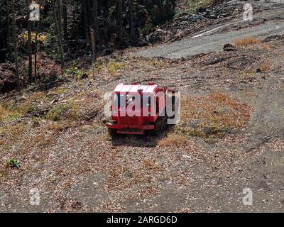 Roter Traktor auf einer felsigen Straße vor dem Hintergrund von Wald und trockenem Laub Stockfoto