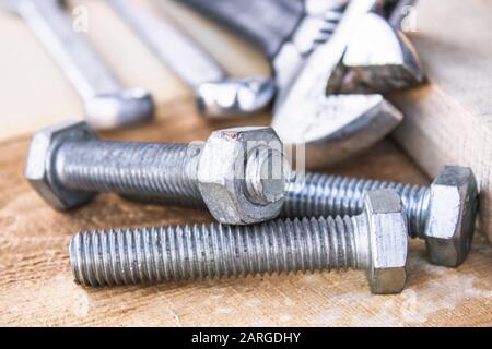 Ein verstellbarer Schraubenschlüssel liegt in der Nähe der Schrauben und Muttern der Unterlegscheibe vor dem Hintergrund von Holzplatten. Das Konzept der Werkzeuge und Reparaturarbeiten. Stockfoto