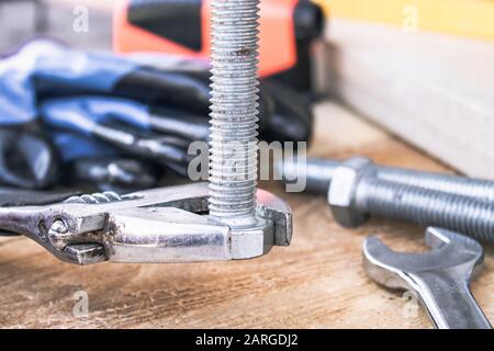 Ein verstellbarer Schraubenschlüssel liegt in der Nähe der Schrauben und Muttern der Unterlegscheibe vor dem Hintergrund von Holzplatten. Das Konzept der Werkzeuge und Reparaturarbeiten. Stockfoto