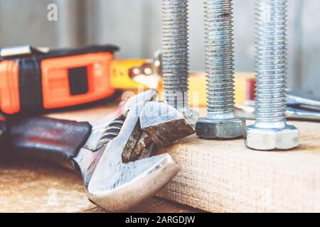 Ein verstellbarer Schraubenschlüssel liegt in der Nähe der Schrauben und Muttern der Unterlegscheibe vor dem Hintergrund von Holzplatten. Das Konzept der Werkzeuge und Reparaturarbeiten. Stockfoto