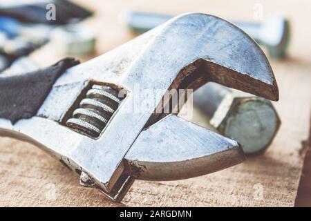 Ein verstellbarer Schraubenschlüssel liegt in der Nähe der Schrauben und Muttern der Unterlegscheibe vor dem Hintergrund von Holzplatten. Das Konzept der Werkzeuge und Reparaturarbeiten. Stockfoto