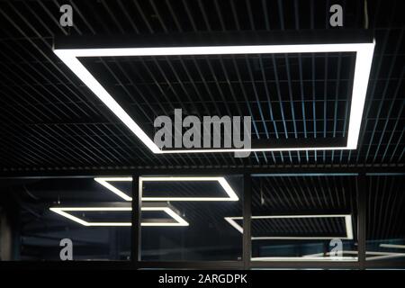 Moderne Bürobeleuchtung. Dünne Lampen in Office dunklen Decke. LED Weiß kaltes Licht über Arbeitsplätze. Stockfoto