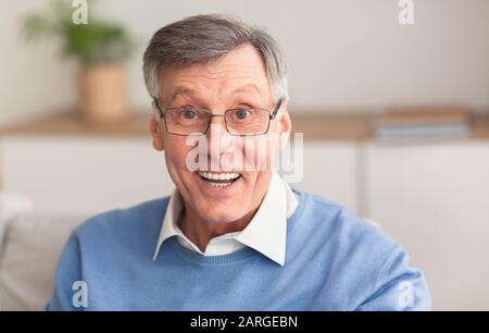 Aufgeregter Älterer Mann, Der Auf Sofa Zu Hause Sitzt Stockfoto