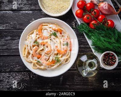 Italienische Pasta Spaghetti mit Garnelen, Behamelsauce und gehacktem Dill auf dunklem rustikalem Holztisch, Draufsicht Stockfoto