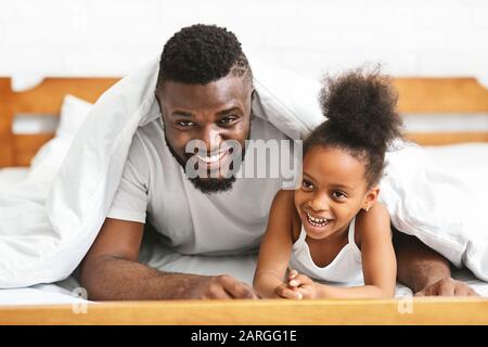 Lächelnder schwarzer Familienvater und Tochter unter Decke legen Stockfoto