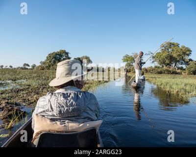 Touristen, die durch das flache Wasser von Mokoro im Okavango-Delta, Botswana, Afrika poliert werden Stockfoto