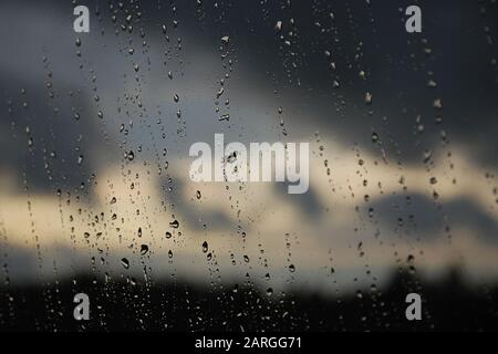 Regentropfen im Fensterbereich. Schwarzer, grauer, weißer Farbverlauf auf unscharfem Hintergrund. Bewölktes Regenwetter außerhalb des Fensters. Kühlung, Regen, schlechtes Wetter Stockfoto