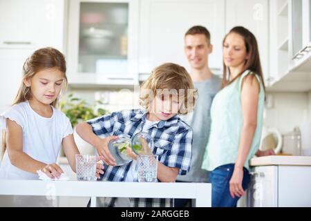 Zwei Kinder trinken in der Küche unter Aufsicht ihrer Eltern Wasser mit frischem Limes Stockfoto