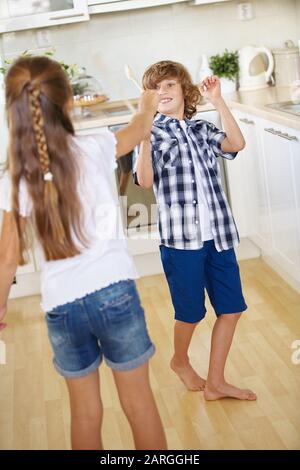 Kinder kämpfen mit Holzlöffeln in der Küche um Spaß Stockfoto