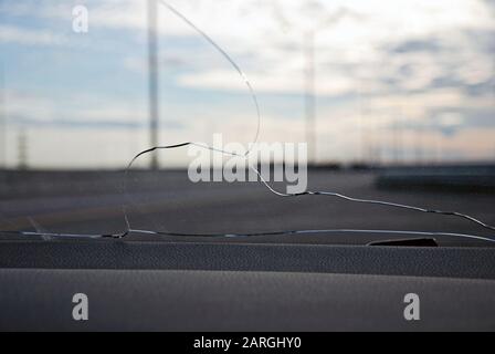 Risse an der Windschutzscheibe des Autos, die von einem Stein getroffen wurden, der unter den Rädern eines anderen Autos ausgeworfen wurde. Blick von innen gegen leere Autobahn Stockfoto