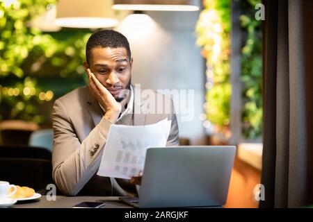 Afro-Geschäftsmann betrachtet Dokumente mit Grafiken Stockfoto