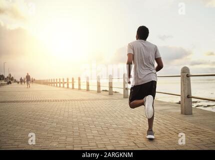 Rückblick auf einen jungen männlichen Sportler, der am Morgen auf der Promenade am Meer läuft Stockfoto